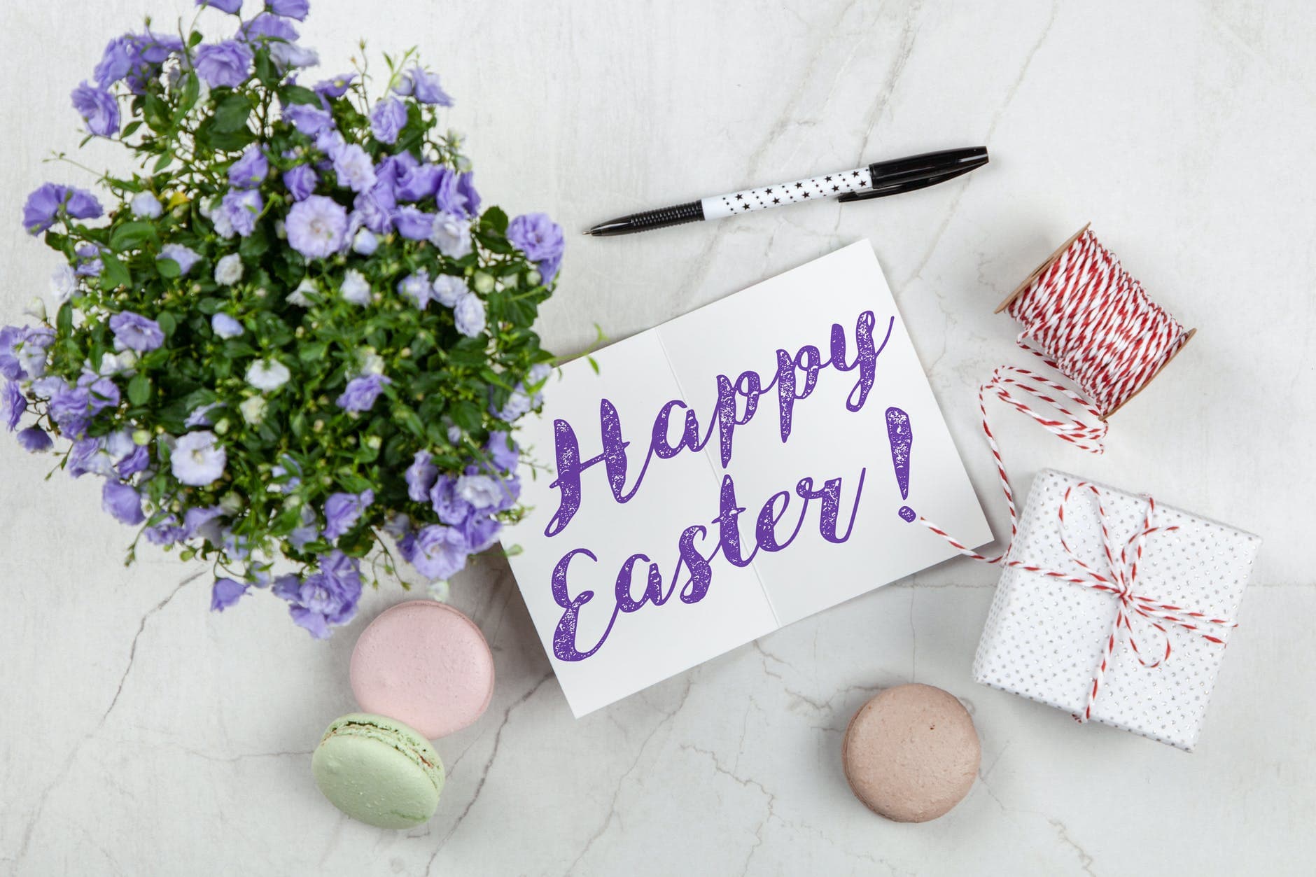 Cartão escrito “Happy Easter!” entre flores lilases, presentes e macarons