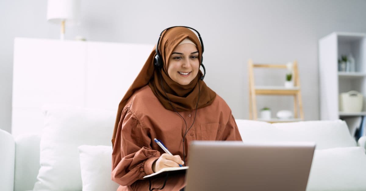 Aluna com fone de ouvido fazendo anotações diante do notebook