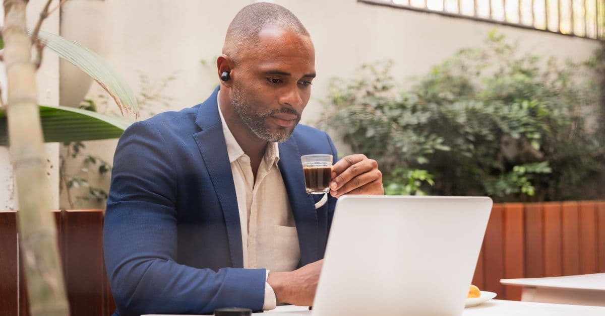Profissional de terno tomando café enquanto trabalha no notebook
