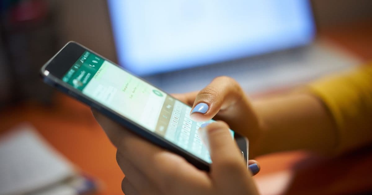 Mãos segurando um celular com uma conversa de WhatsApp aberta